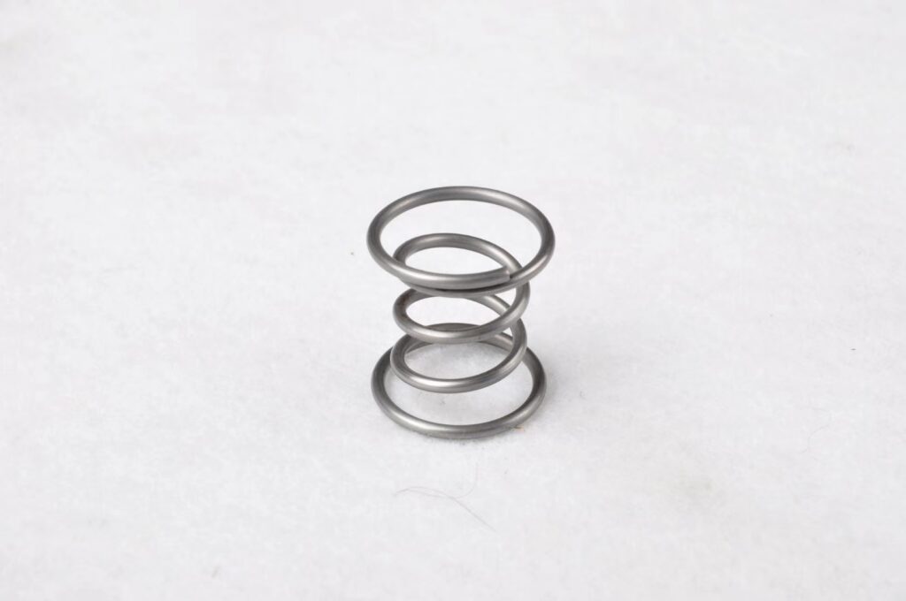 A small stainless steel conical spring with coils that narrow toward one end.