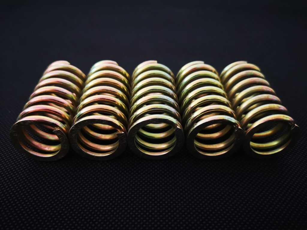 Five yellow zinc plated helical compression springs lying side by side on a black surface, seen from one end