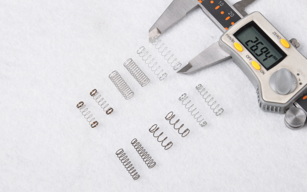 Small springs laid out beside a digital caliper.