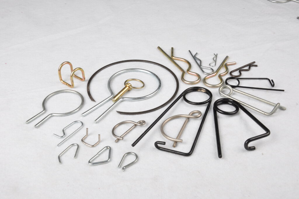 An assortment of wire forms in zinc, yellow zinc and black, including R-pins, a lynch pin, retaining rings, clips and formed springs with torsion loops