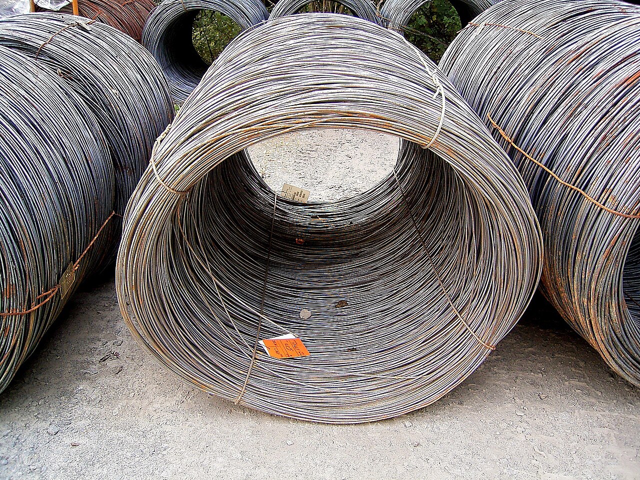 Large coils of steel wire stored outdoors, with steel binding straps and orange identification tags