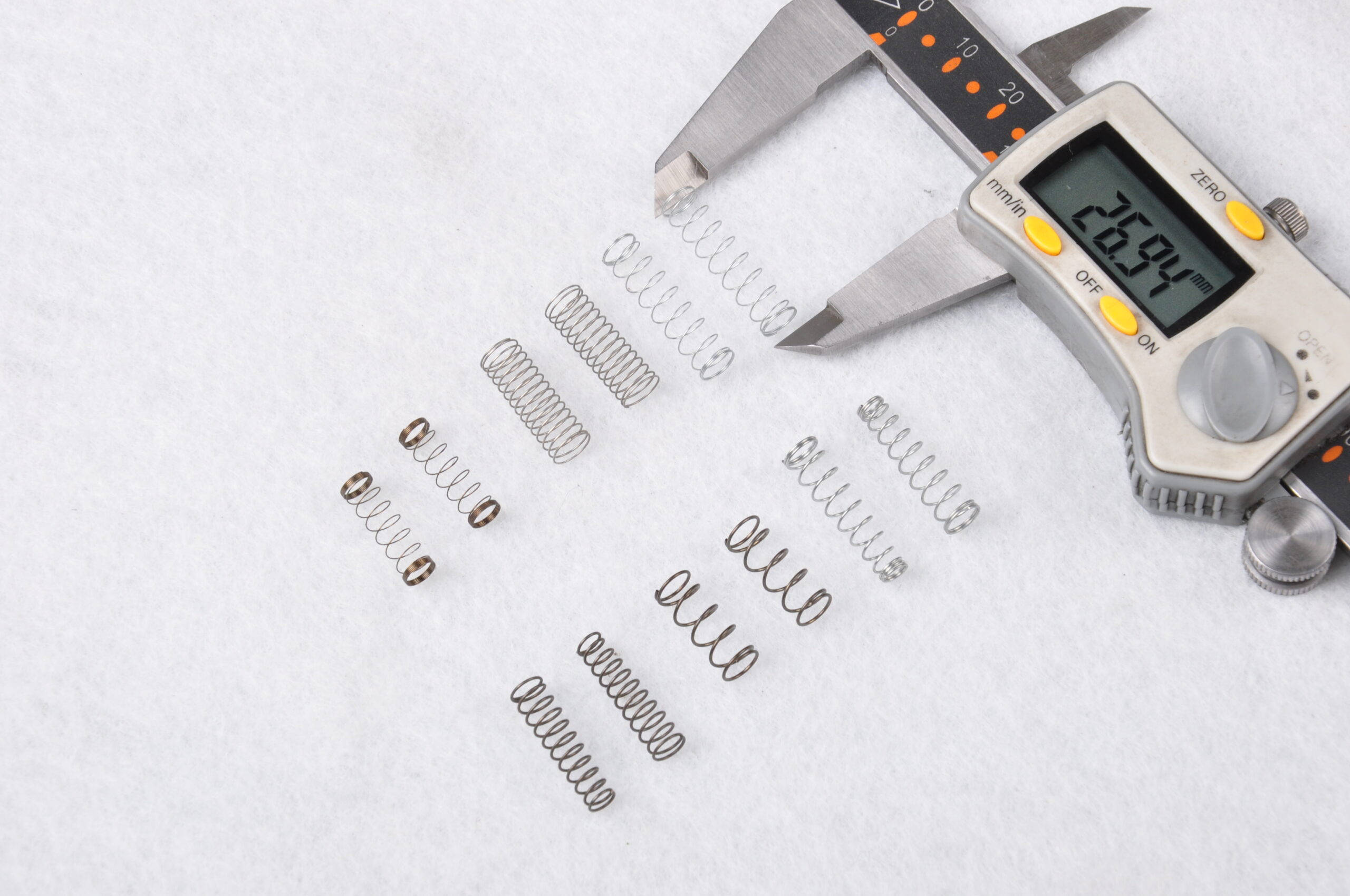 Several small compression and extension springs laid out next to a digital caliper
