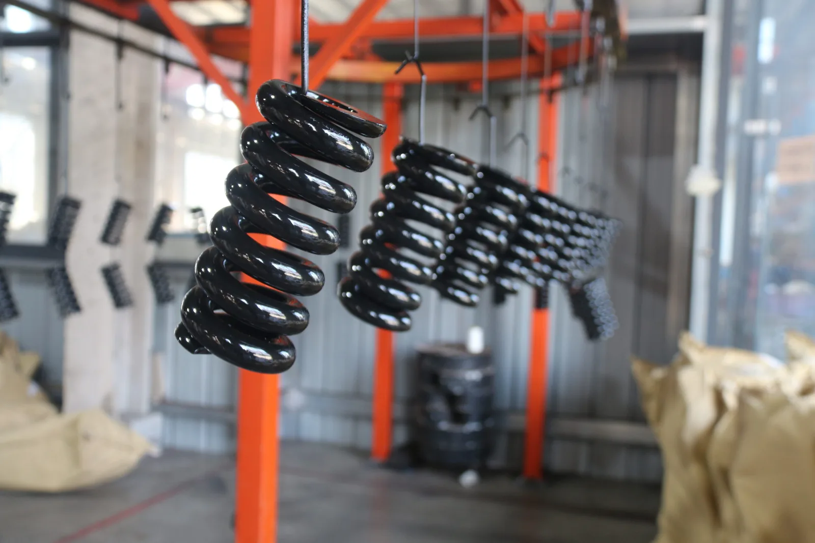 Black coated compression springs hanging from hooks on an overhead conveyor in a coating line