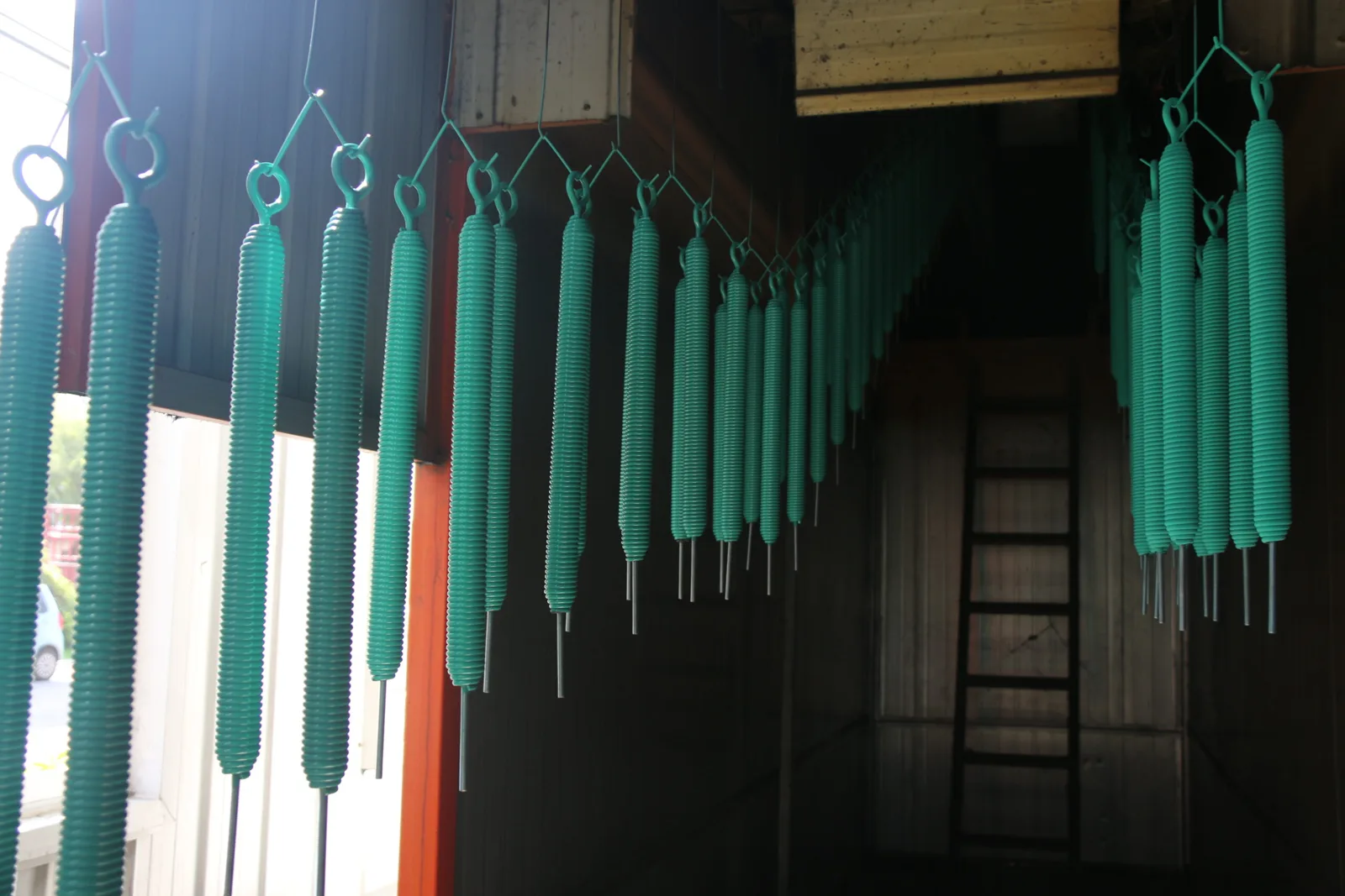 Green coated extension springs with eye ends hanging in rows on an overhead coating line