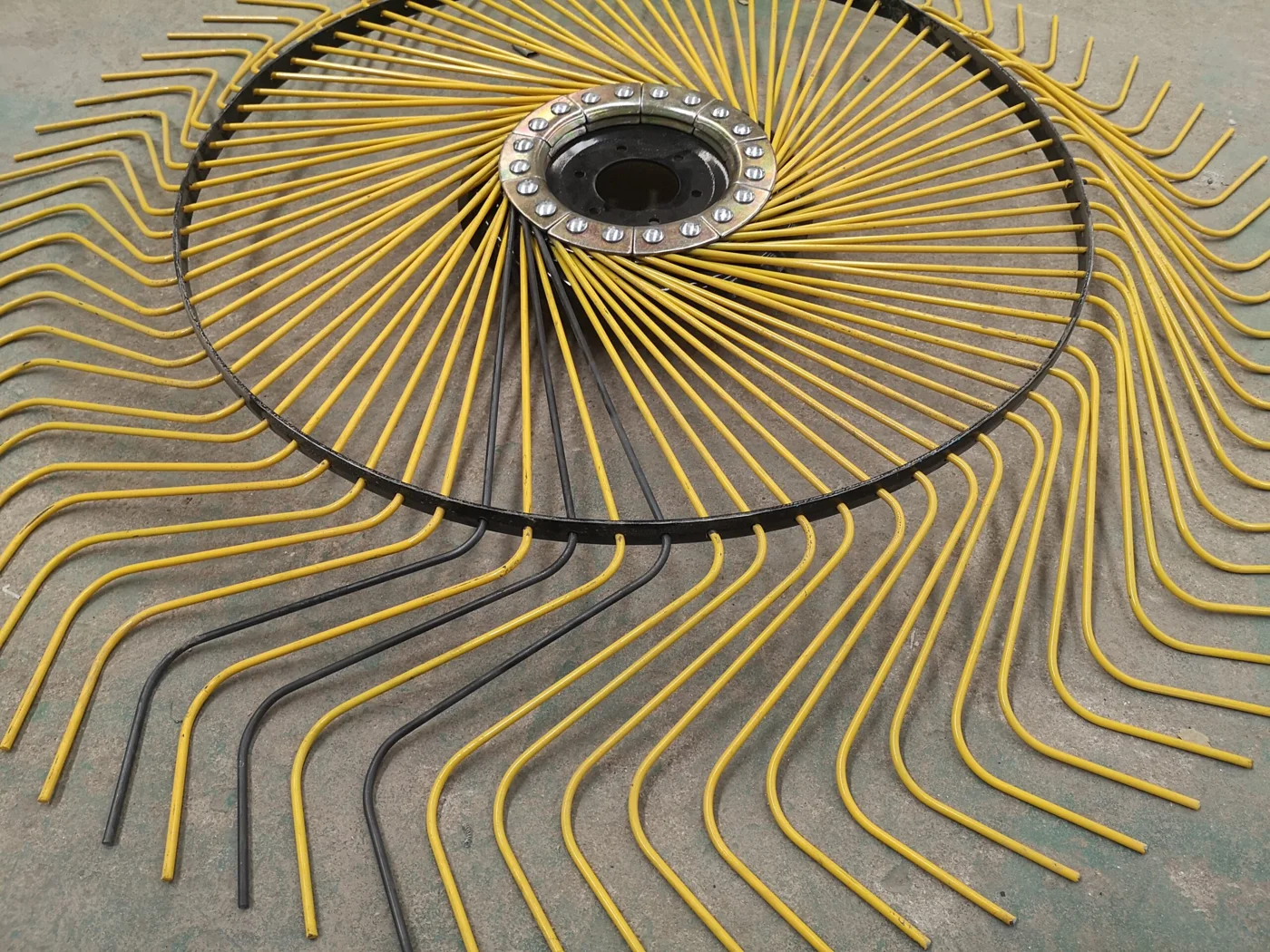 A rake wheel with yellow and black wire fingers fitted through its rim, laid on a workshop floor
